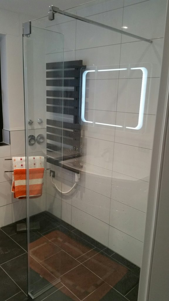 In der Duschabtrennung aus Glas spiegelt sich die Ringbeleuchtung des Waschtischunterschrankes