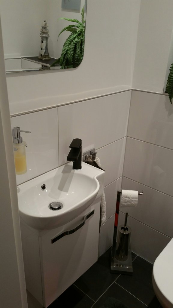 Gästewaschbecken mit Waschbeckenunterschrank, darüber ein Design Spiegel mit abgerundeten Ecken und gefarster Kante